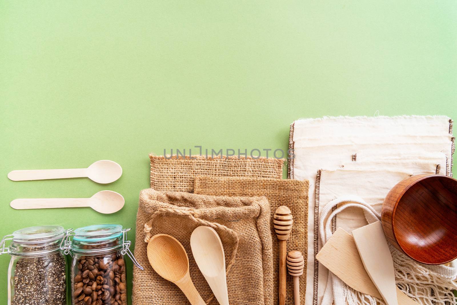 Zero waste eco friendly bags and wooden tools top view on green background with copy space