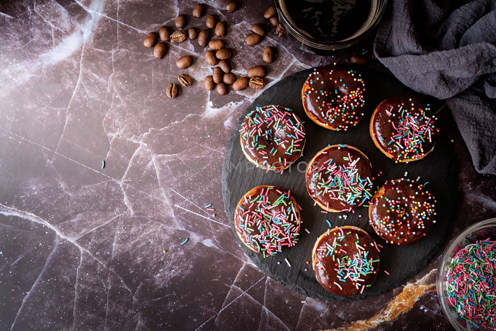 Fresh donuts with chocolate glaze and colorful sprinkles on dark background, top view copy space
