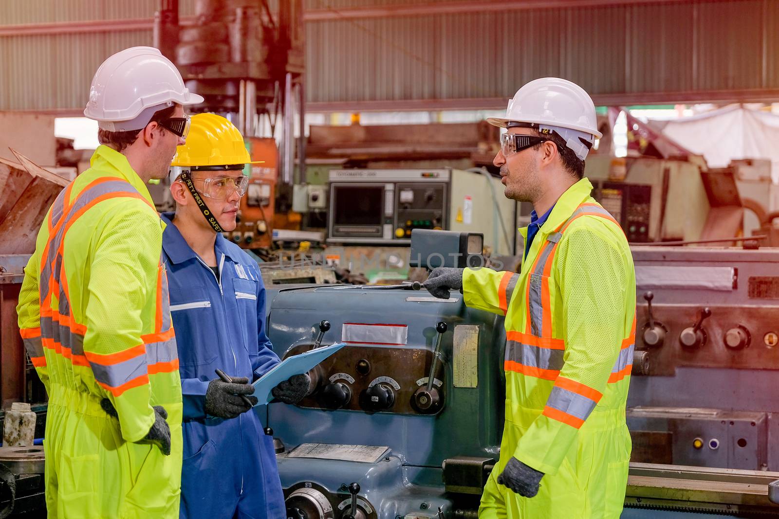 Two yellow uniform technician man with blue uniform work together as team to maintenance and check the machine working in factory.