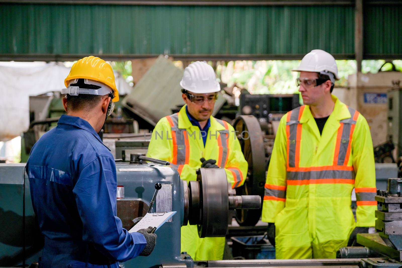 Two yellow uniform technician man with blue uniform work together as team to maintenance and check the machine working in factory.