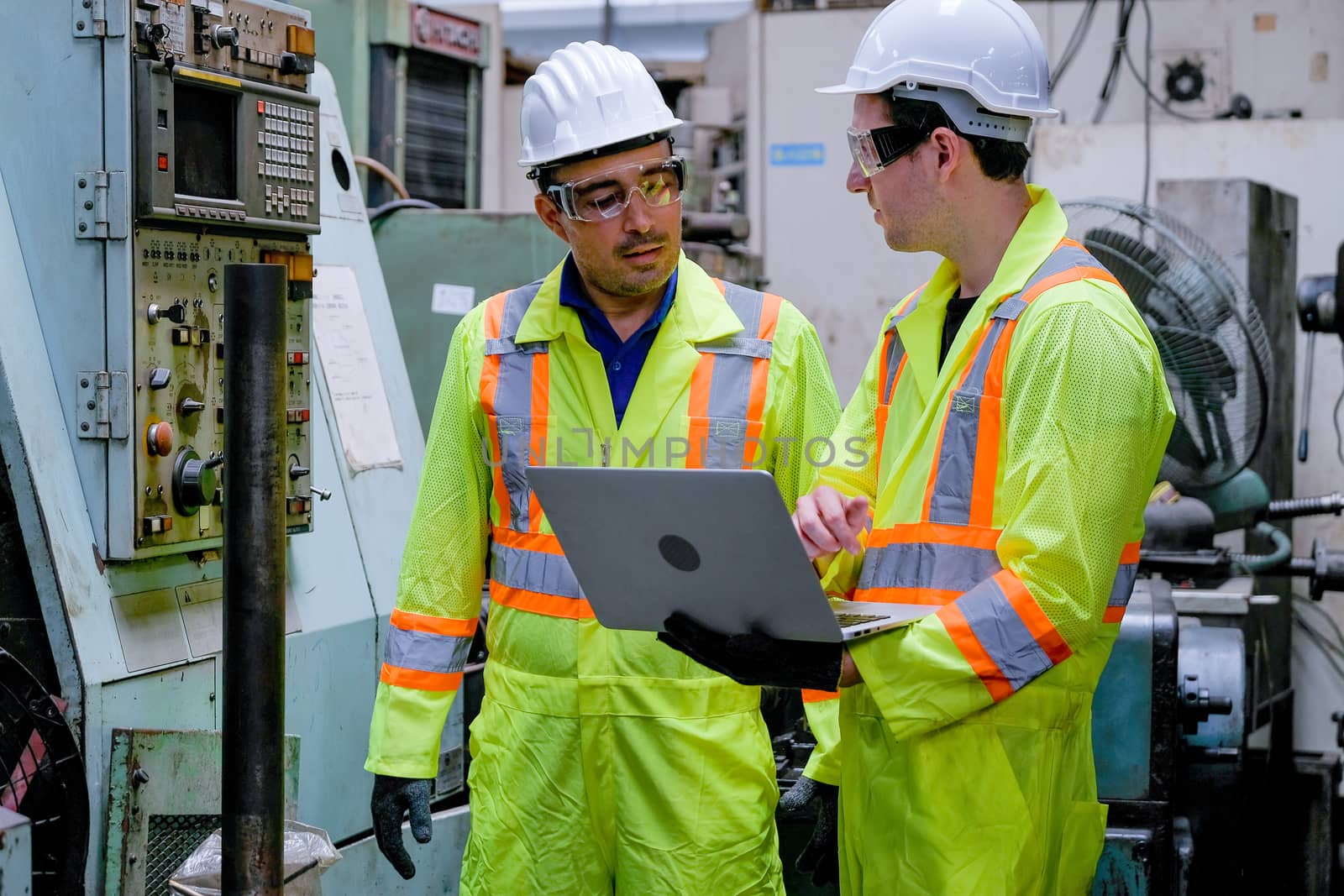 Two technician men with safety uniform discuss about the machine function in factory. by nrradmin