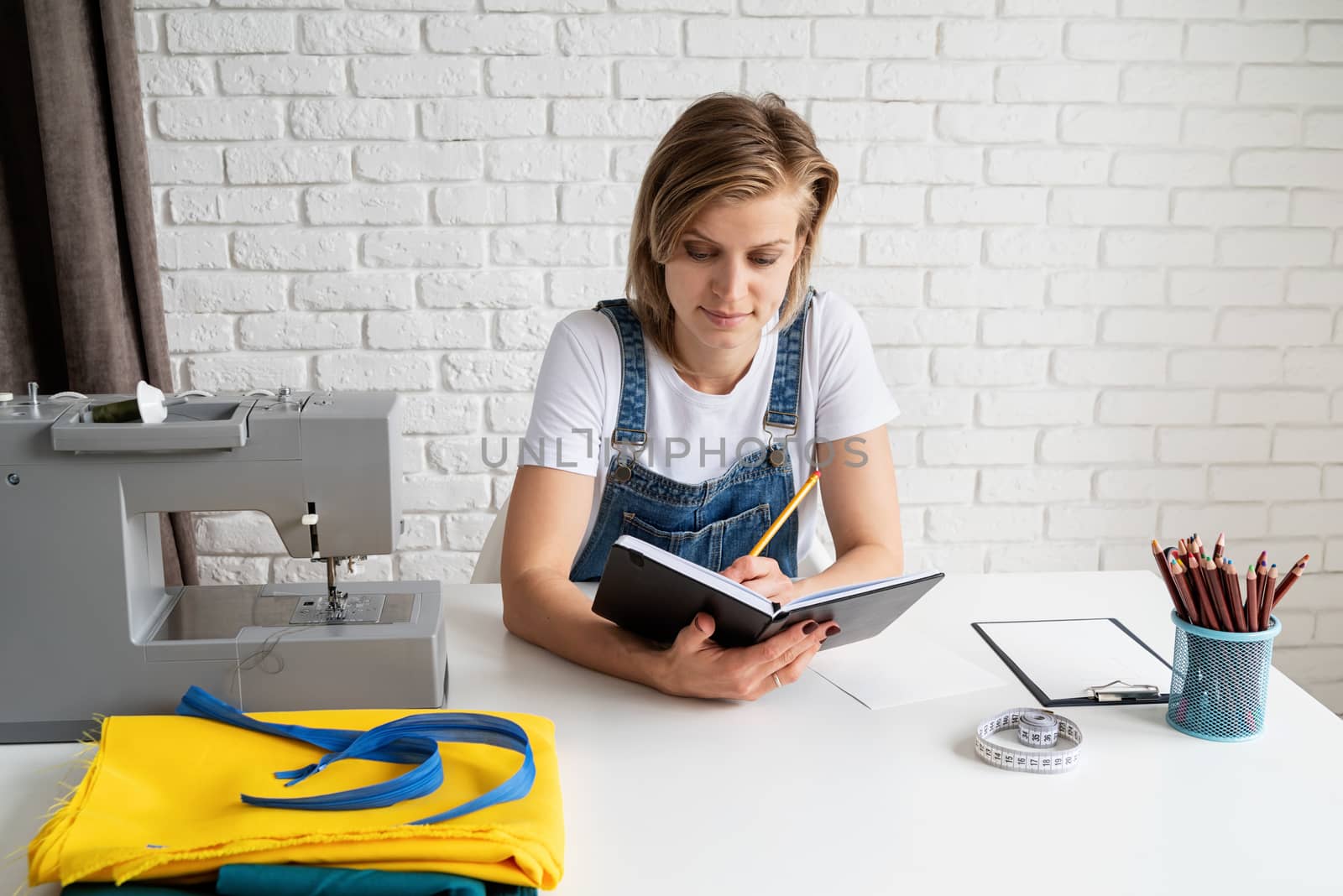 Young blond woman tailor drawing a sketch ready to sew by Desperada