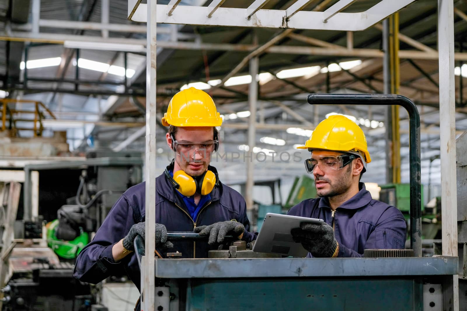 Two technician men with blue uniform and yellow helmet work with the machine in factory. by nrradmin