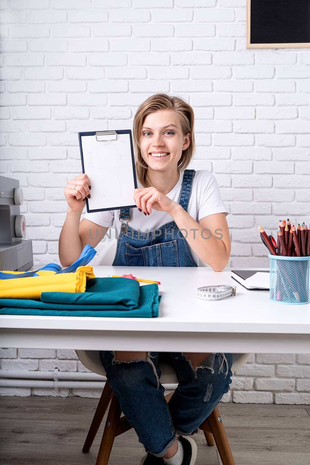 Young blond woman tailor showing a sketch ready to sew a pillow by Desperada