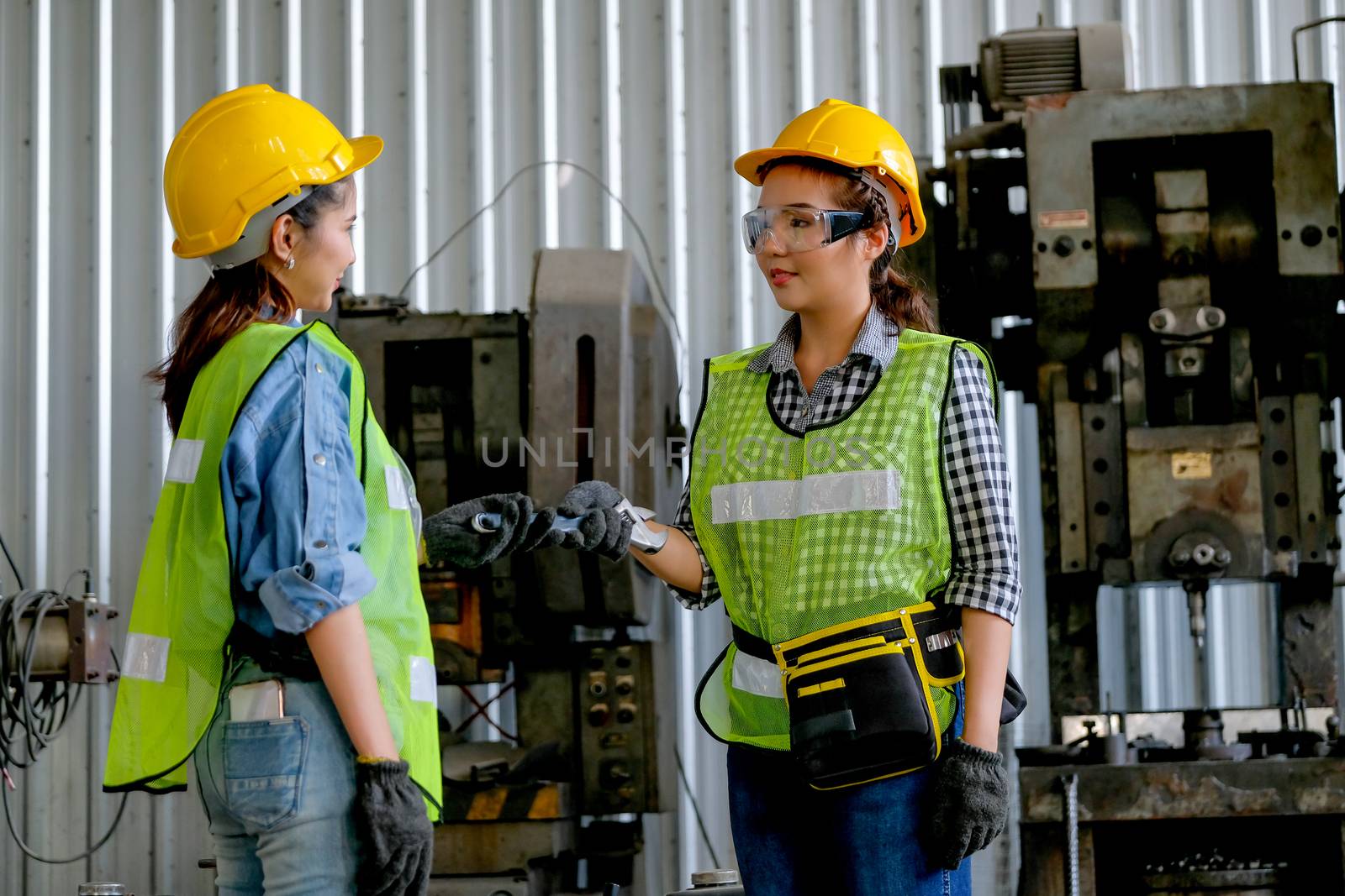 Factory woman technician or engineer worker give wrench to her co-worker in front of machine with day light assign by manager. Concept of good system and manager support  better industrial business.