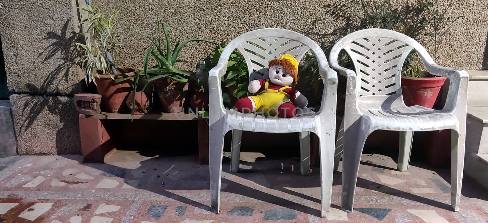 A stuffed doll sitting on a plastic chair alone in backyard in India by mshivangi92
