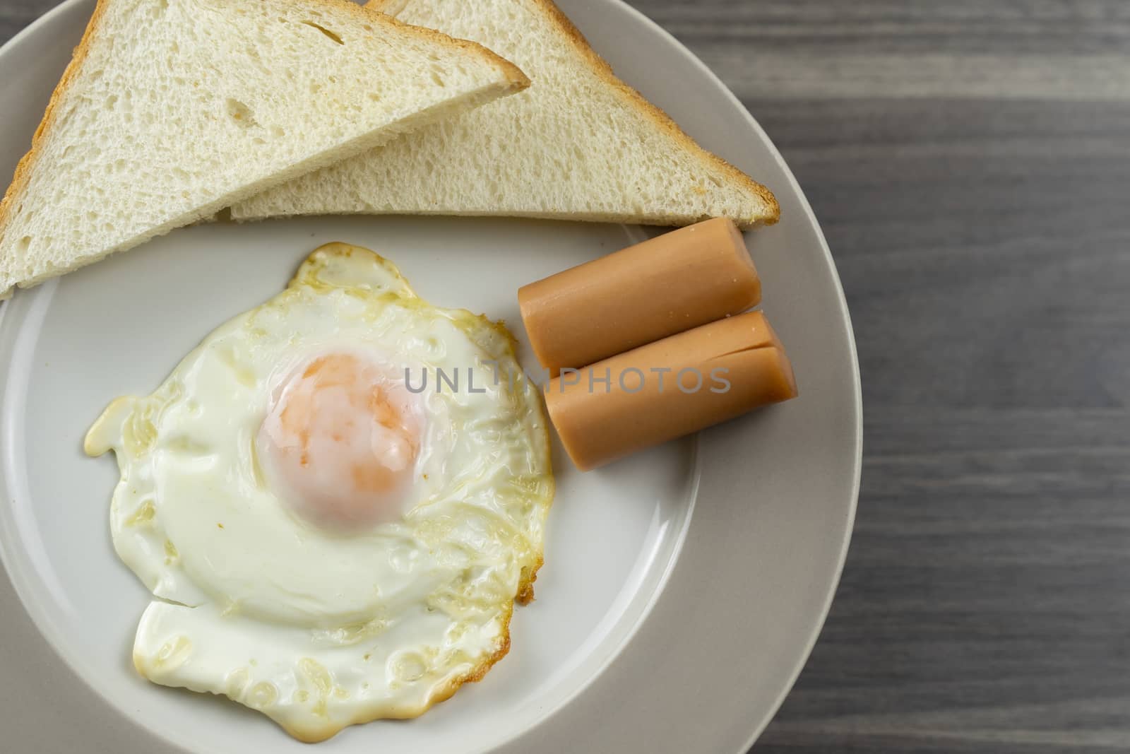 Close-up of breakfast on a white plate in the left corner of the wooden floor

