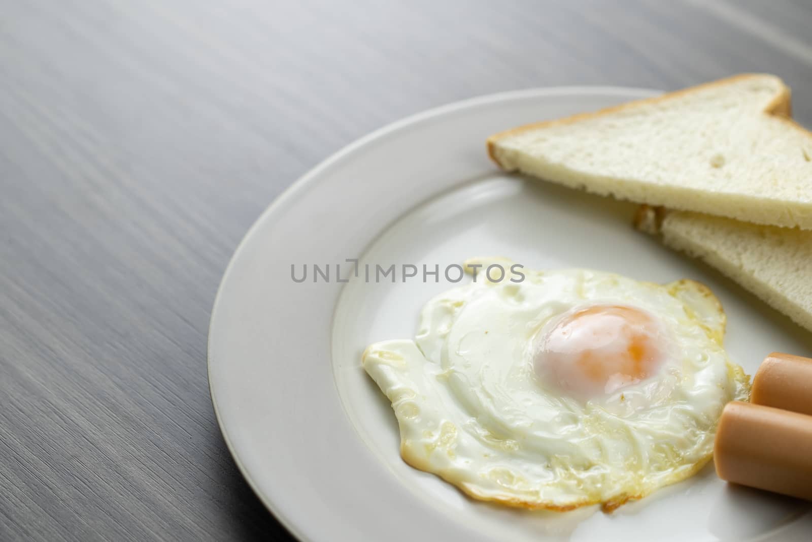 Close-up of breakfast on a white plate in the bottom right corner of the wooden floor