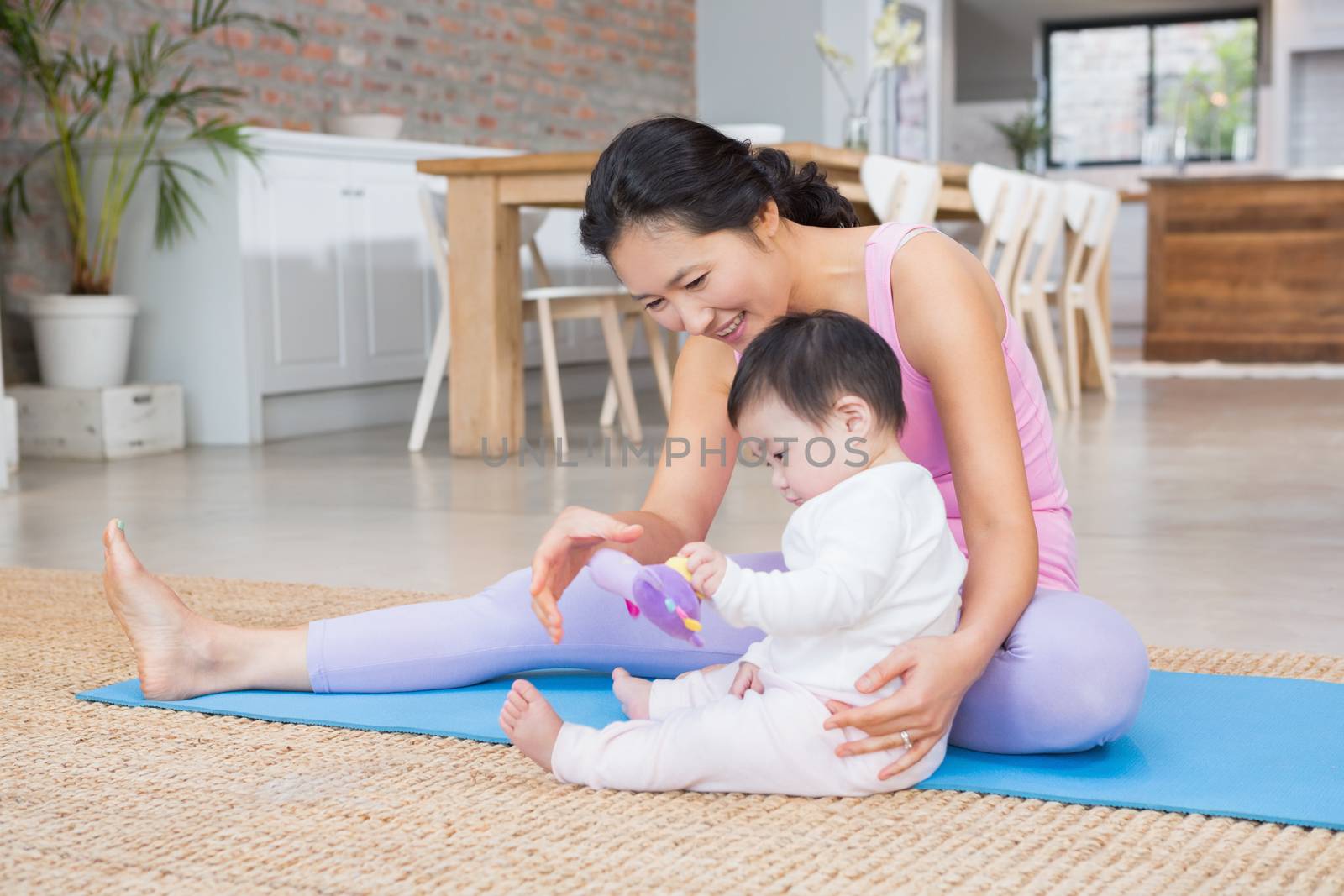 Happy mother and baby daughter sitting on exercising mat at home