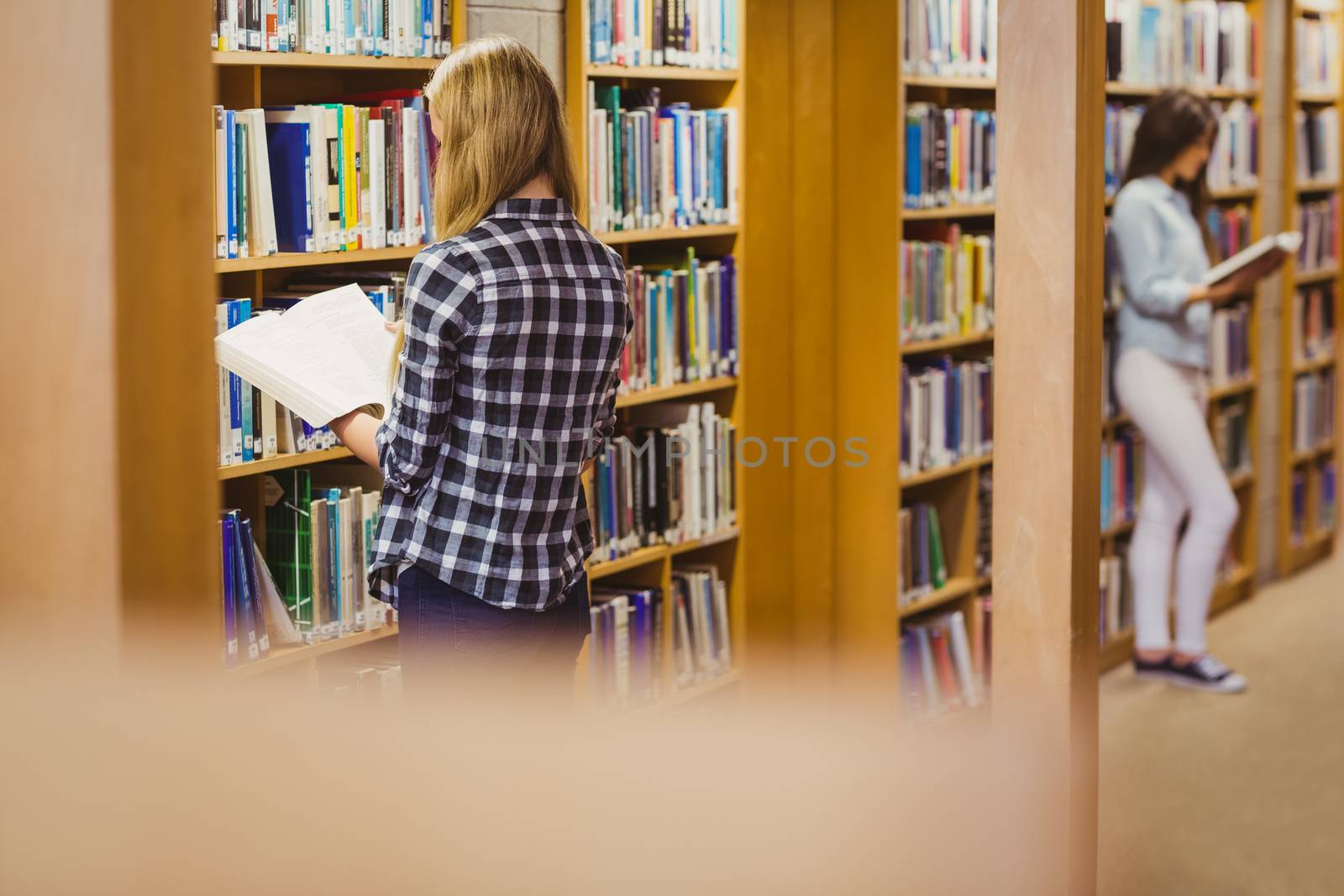 Serious students reading next to bookshelf in library