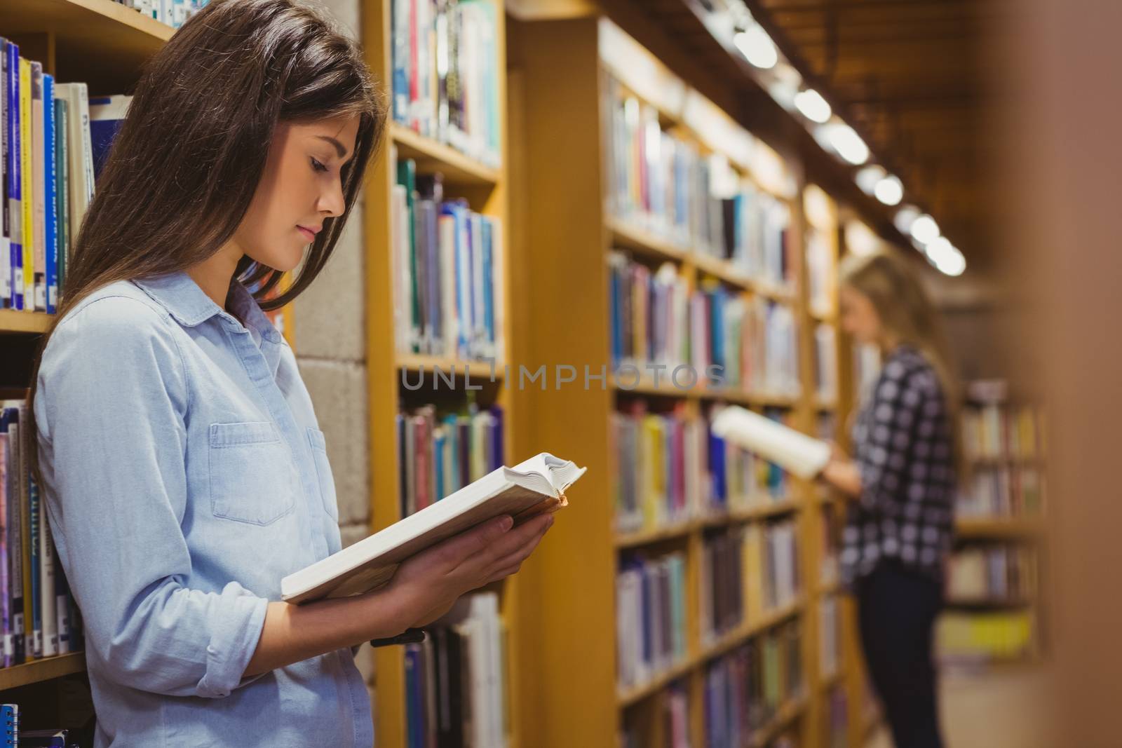 Serious students reading next to bookshelf in library