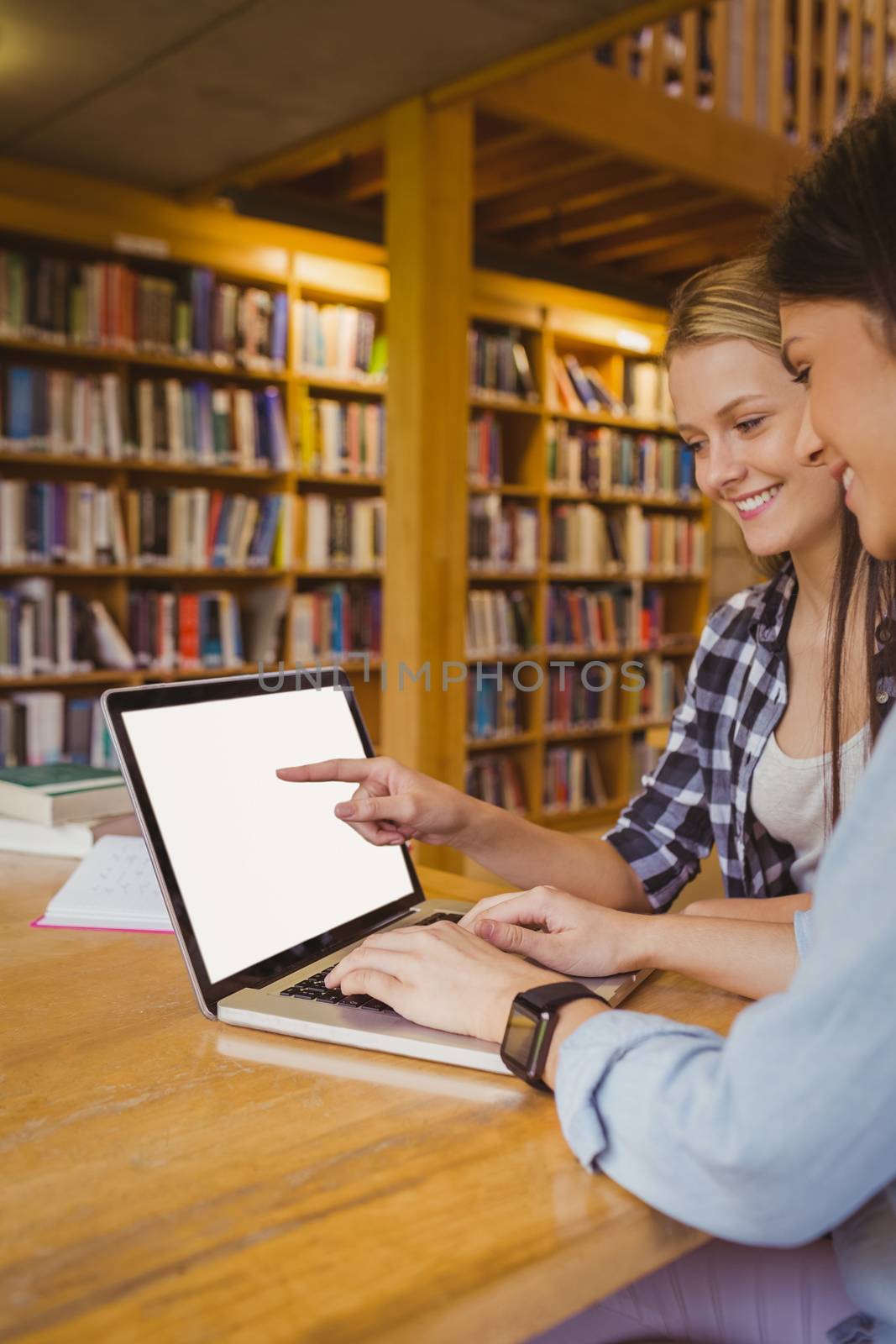 Smiling students using laptop in library 