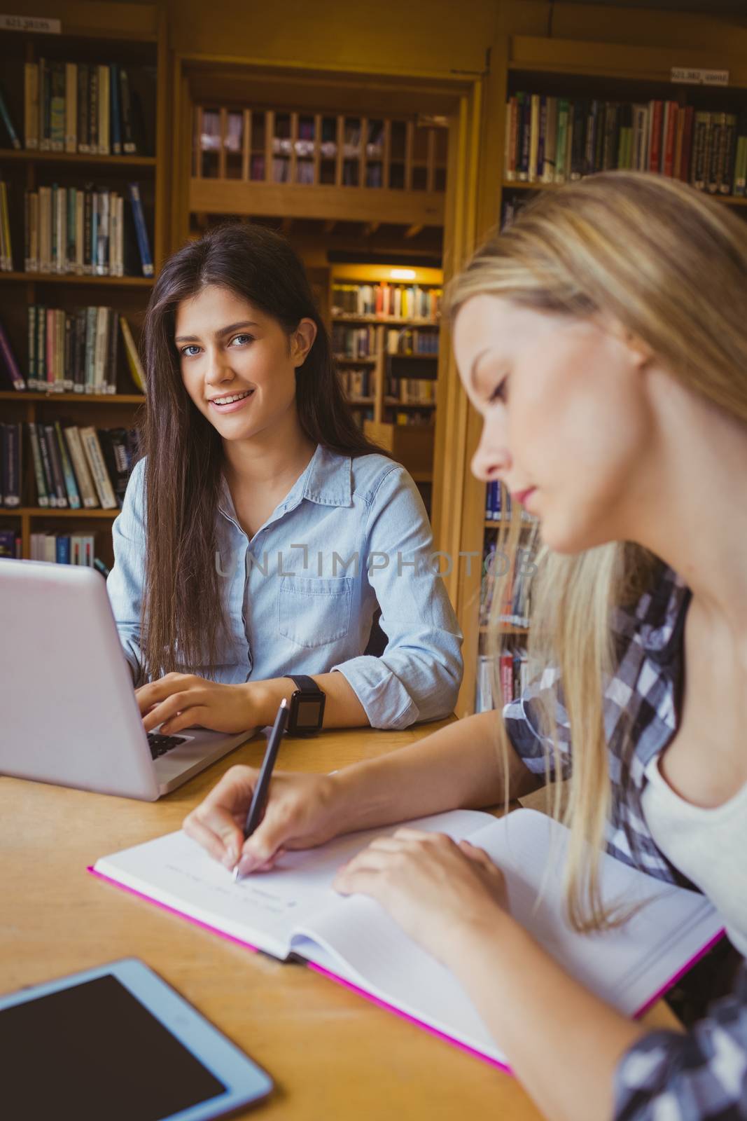 Smiling students using laptop in library 