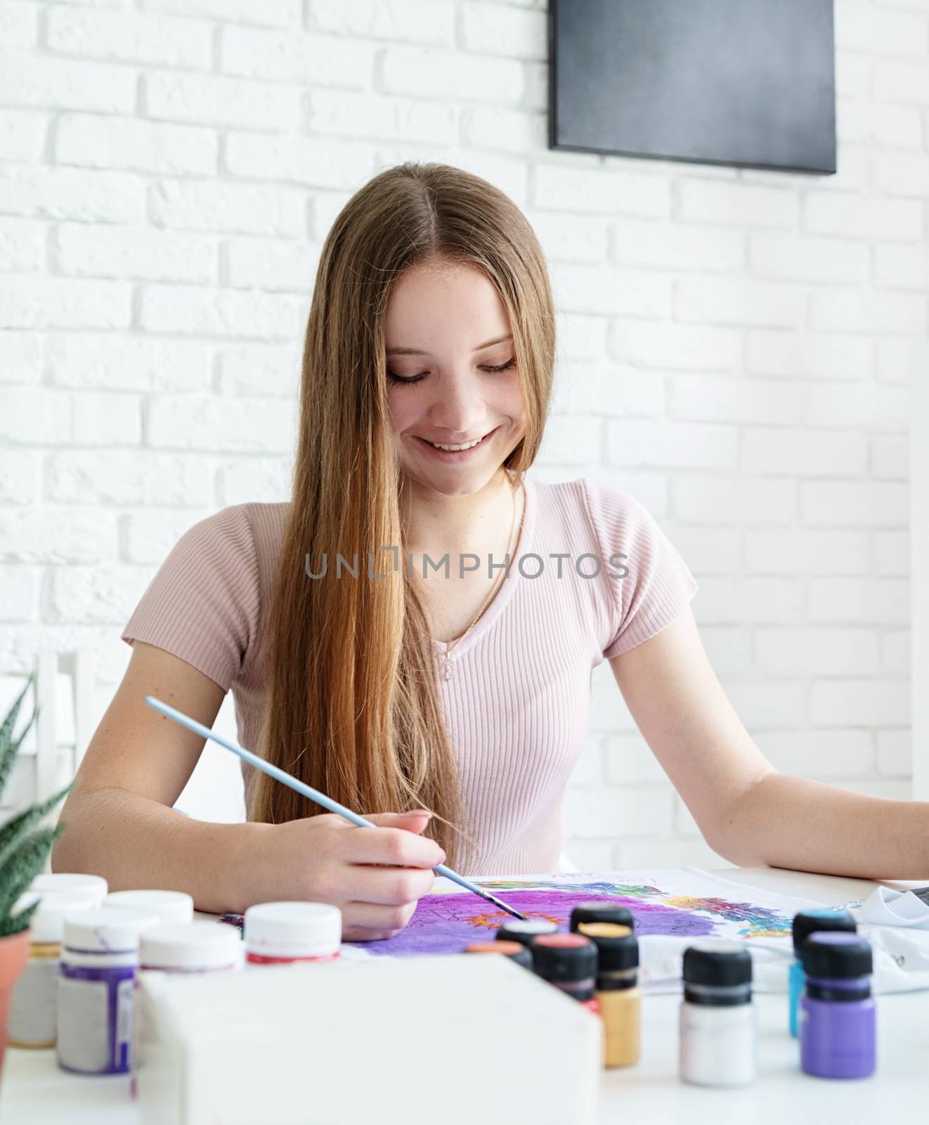 smiling woman artist painting on clothes in her studio by Desperada
