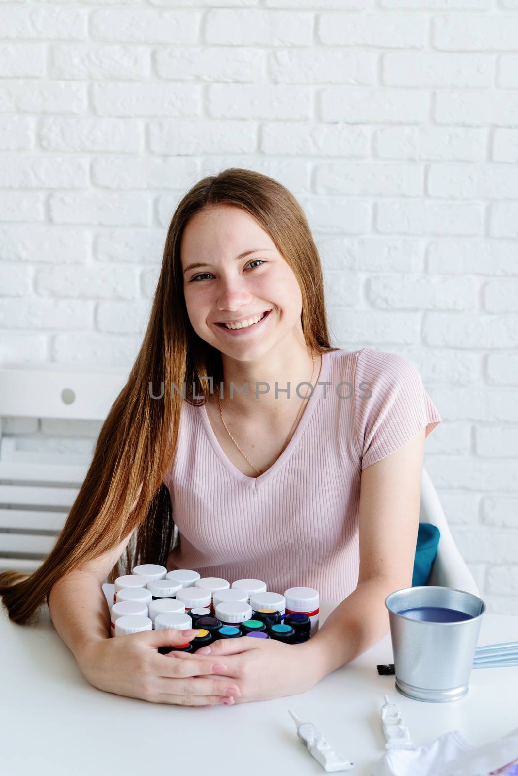 smiling woman artist holding a pile of paint bottles working in her studio by Desperada