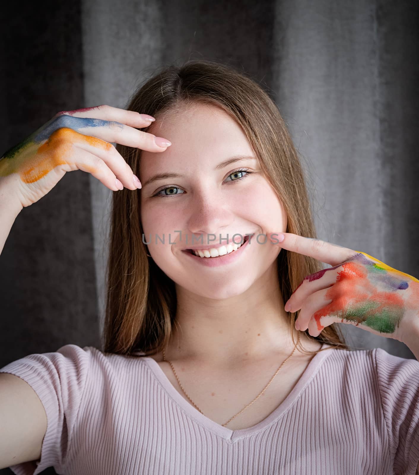 Smiling teenage artist with hands colored with paint