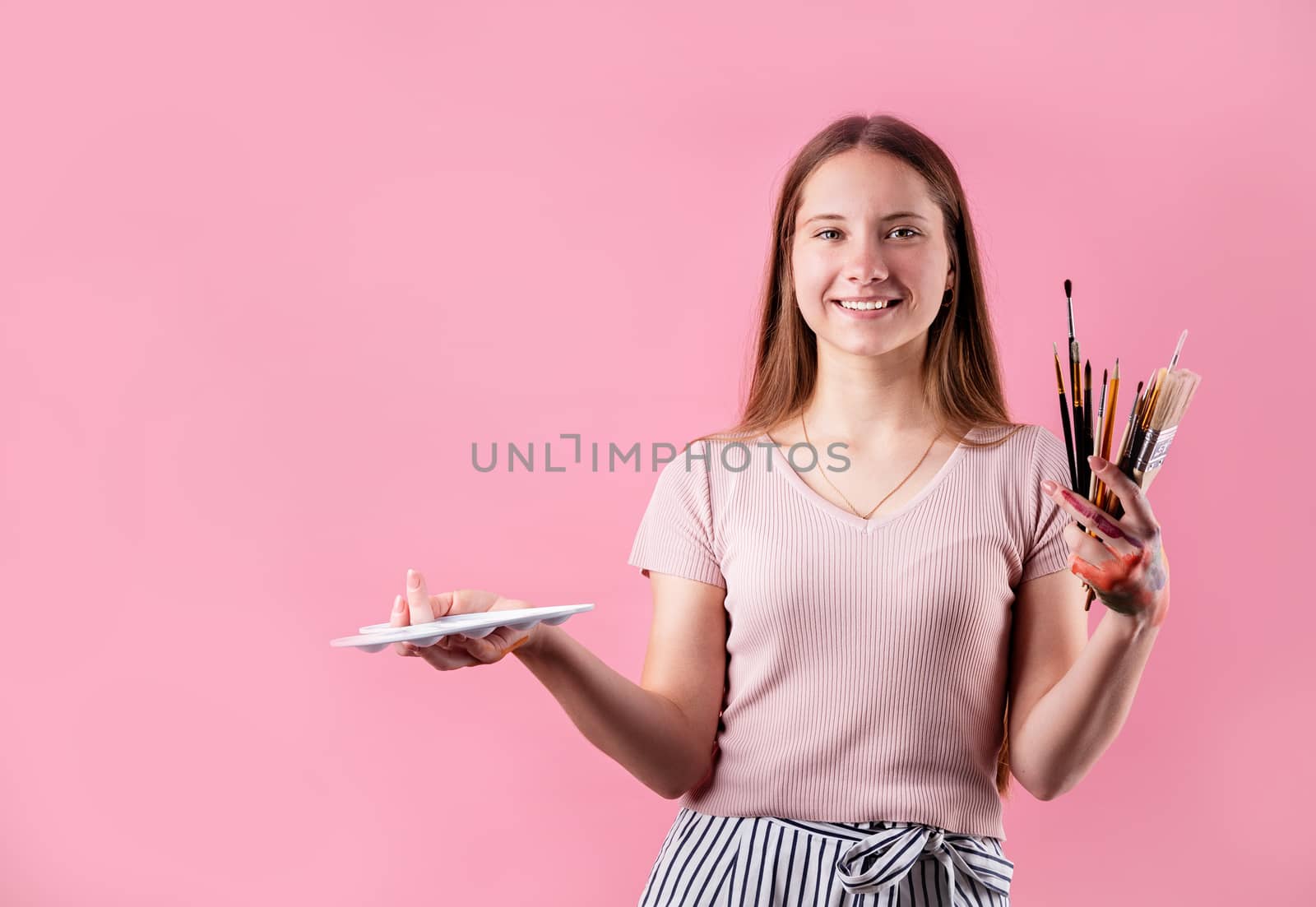 woman artist with a color palette and paintbrushes isolated on pink background by Desperada