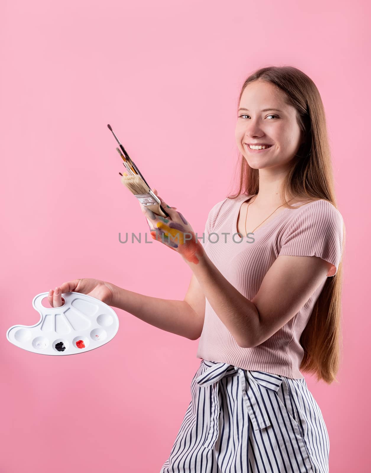 woman artist with a color palette and paintbrushes isolated on pink background by Desperada