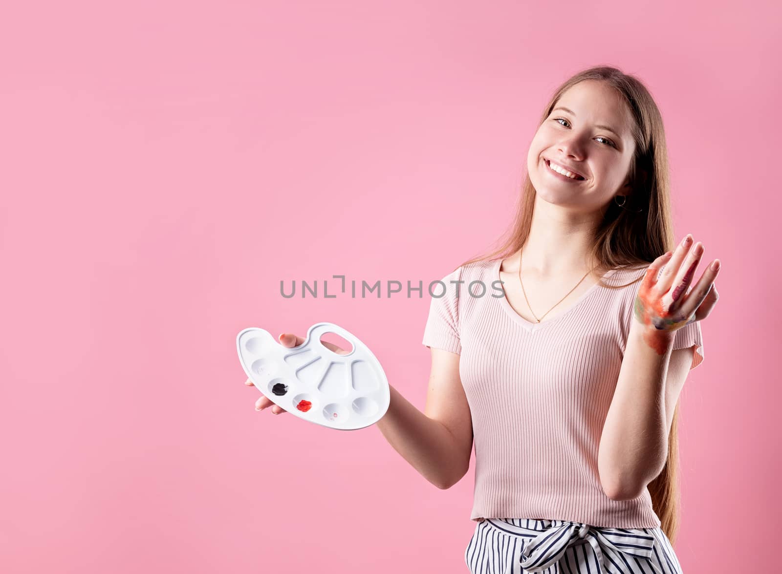 woman artist with a color palette and paintbrushes isolated on pink background by Desperada