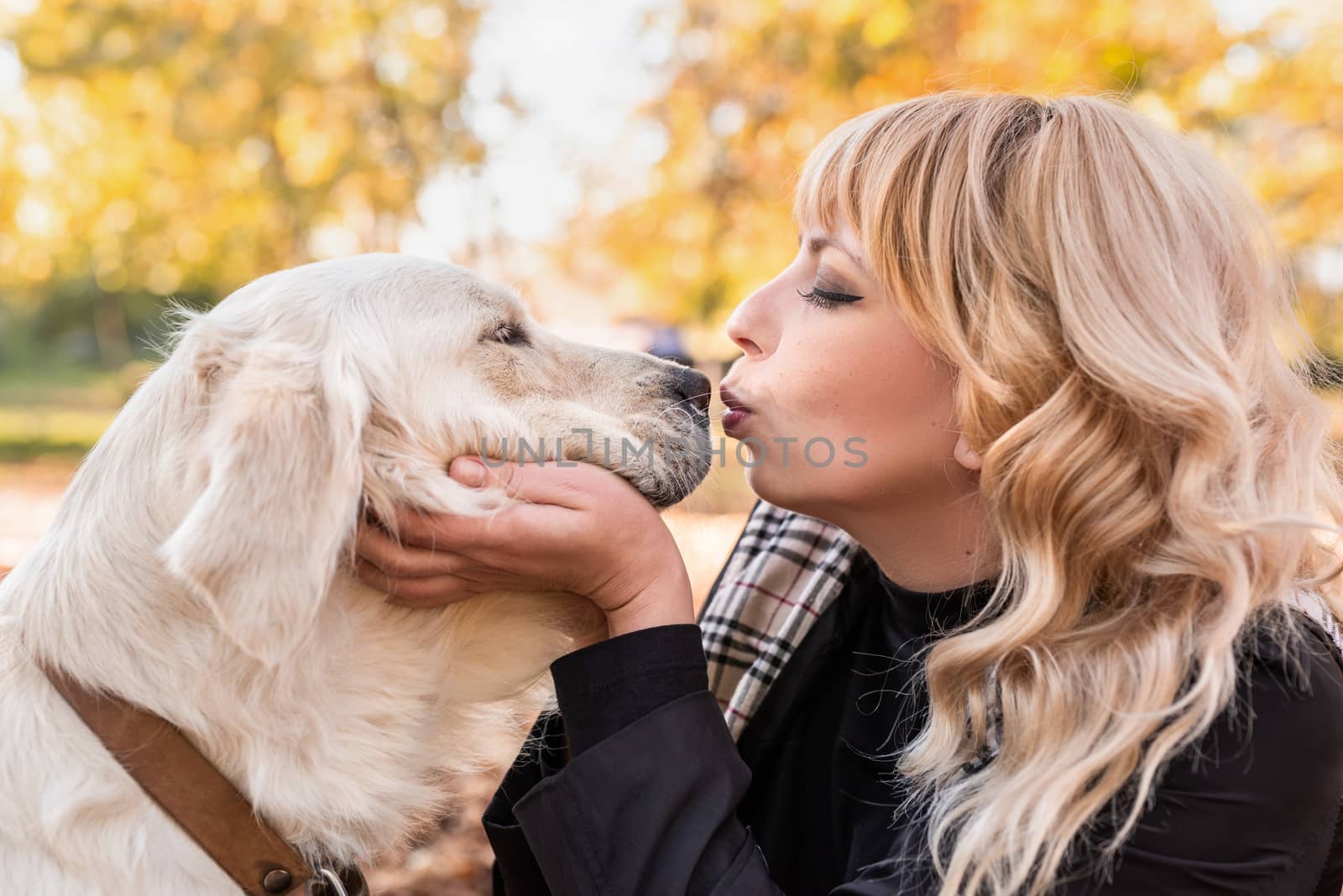 Pet care concept. Happy blond woman kissing her retriever dog in autumn park
