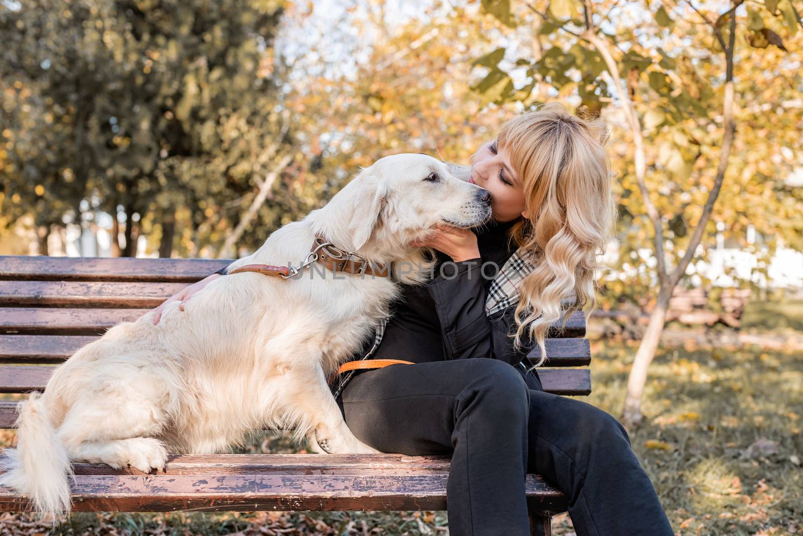 blond caucasian woman sitting with her golden labrador retriever dog on the bench in the park by Desperada