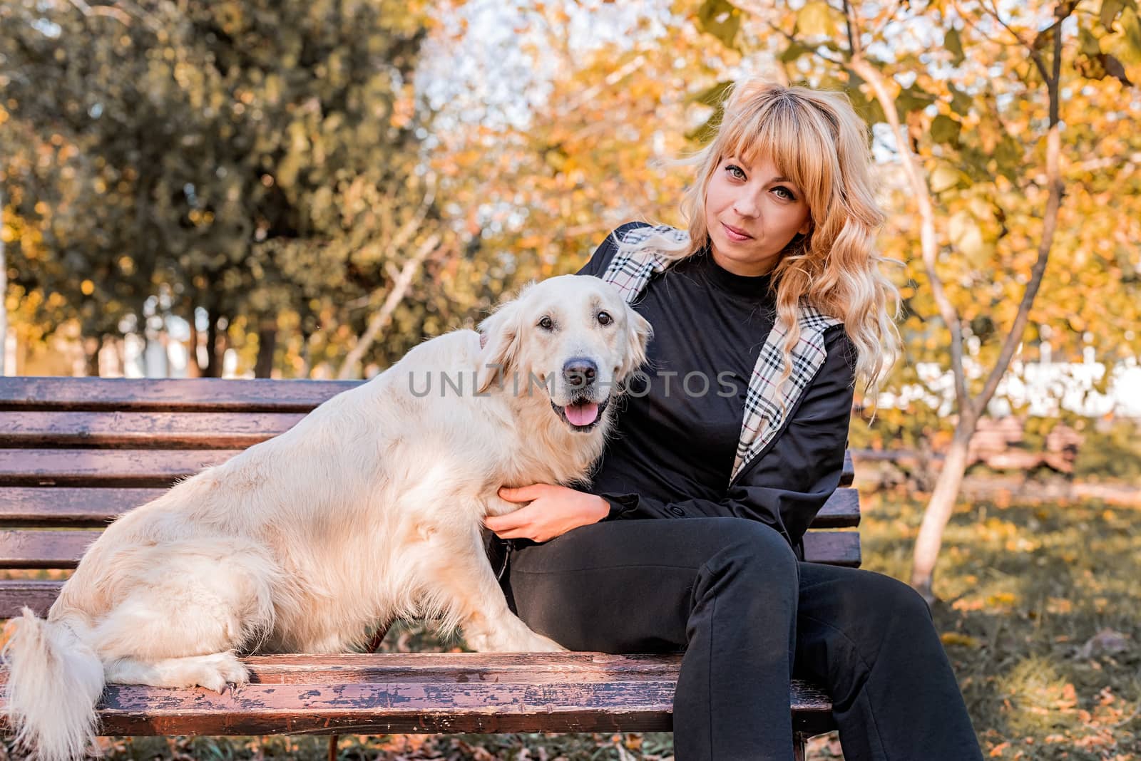 Pet care concept. Young blond woman with her retriever dog on the bencj in the park