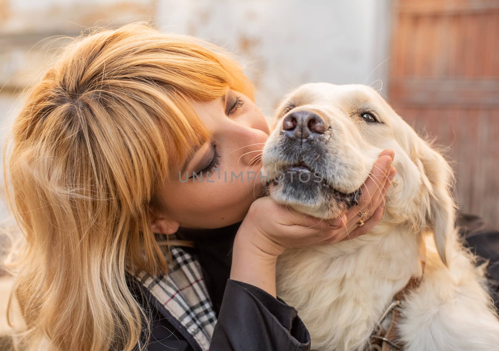 Pet care concept. Blond caucasian woman kissing her golden retriever dog outdoors