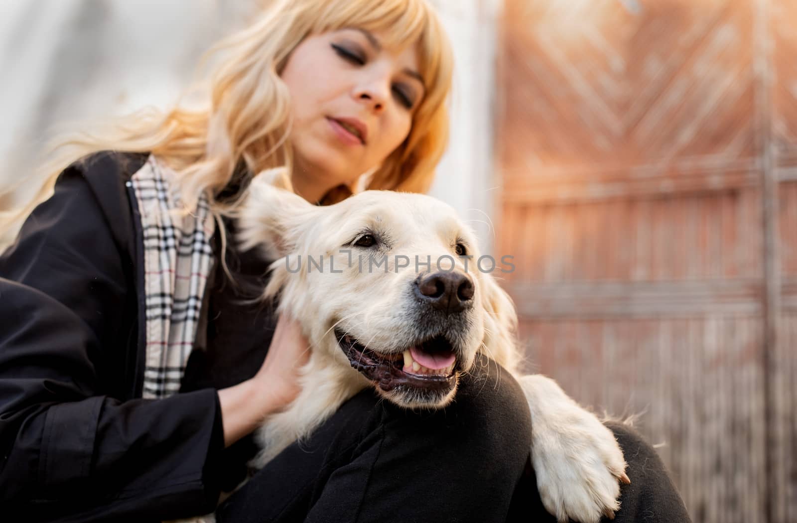 Pet care concept. Blond caucasian woman hugging her golden retriever dog outdoors