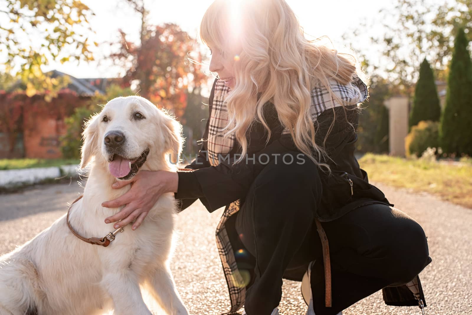 Pet care concept. Blond caucasian woman hugging her golden retriever dog outdoors in the sunset