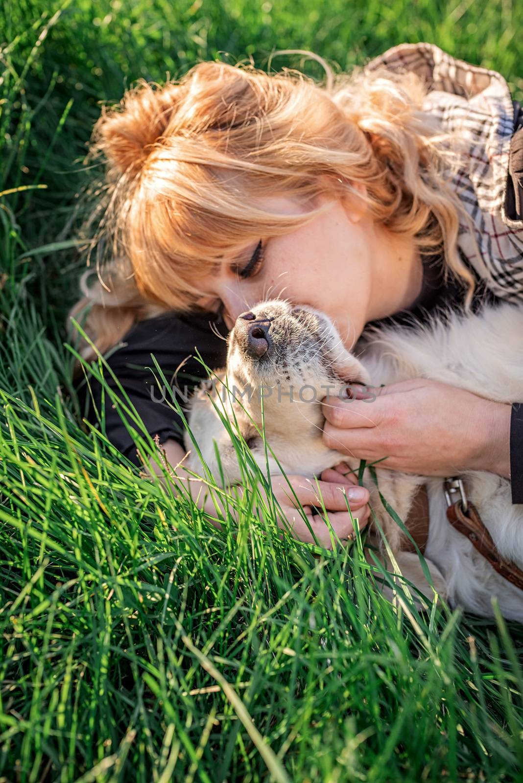 Beautiful caucasian woman laying in the grass with her golden labrador retriever dog at a park in the sunset by Desperada