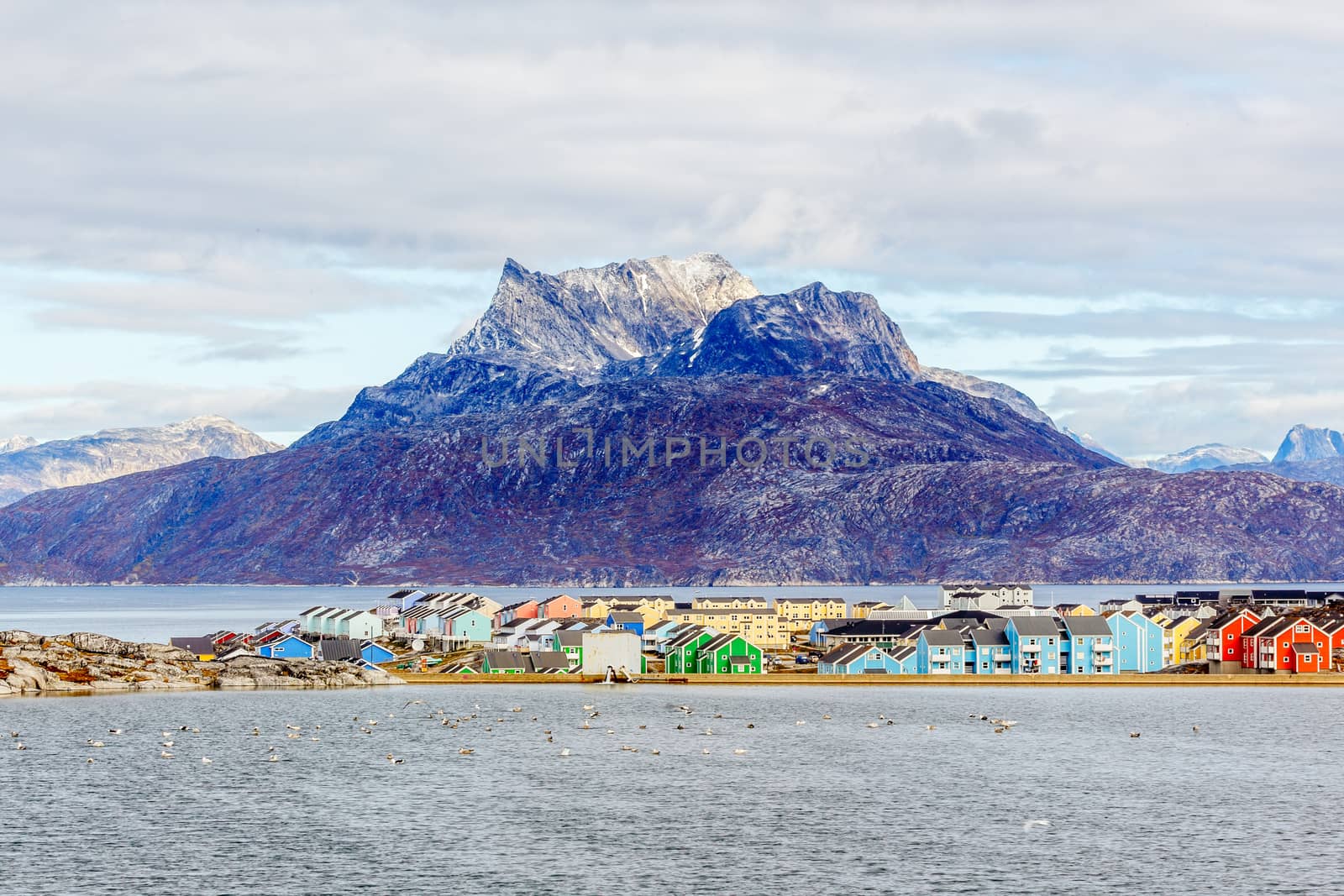 Colorful Inuit buildings in residential district of Nuuk city with lake in the foreground and snow peak of Sermitsiaq mountain, Greenland