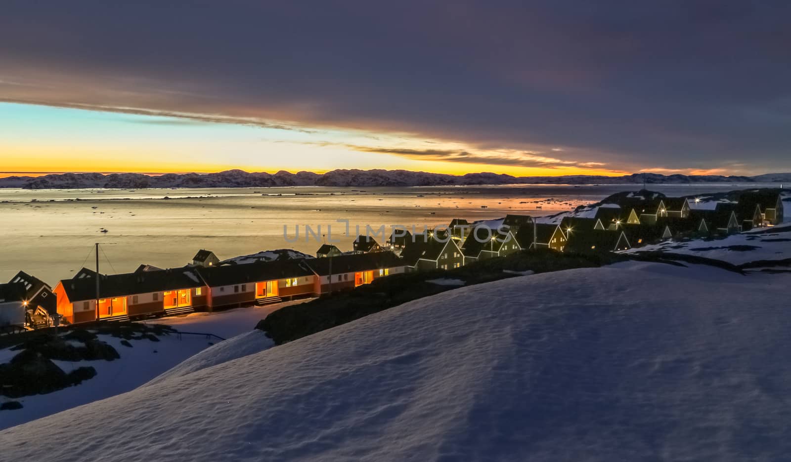 Frozen inuit houses among rocks and snow at the sunset fjord in outskirts of arctic capital Nuuk, Greenland