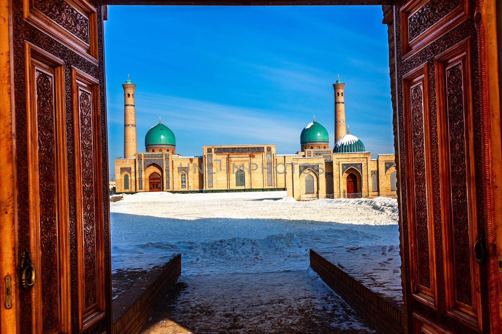 Winter shot of blue domes, mosques and minarets of Hazrati Imam medrese with wooden ornated doors in the foreground, religious center of Tashkent, Uzbekistan