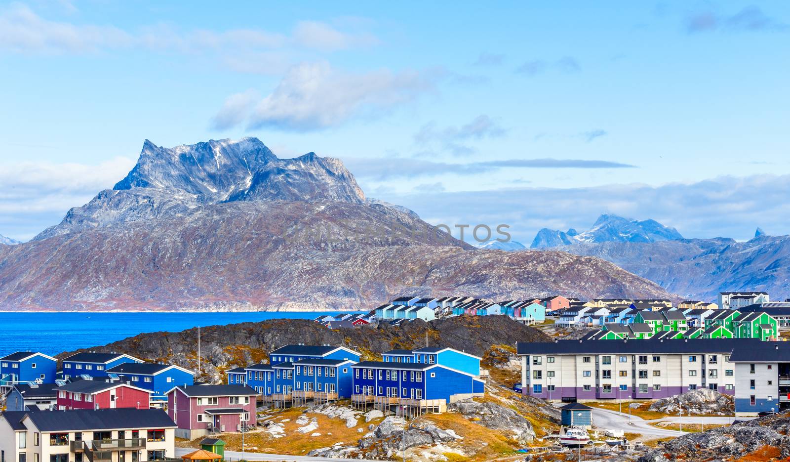 Inuit houses and cottages scattered across tundra landscape in residential suburb of Nuuk city with fjord and mountains in the background, Greenland