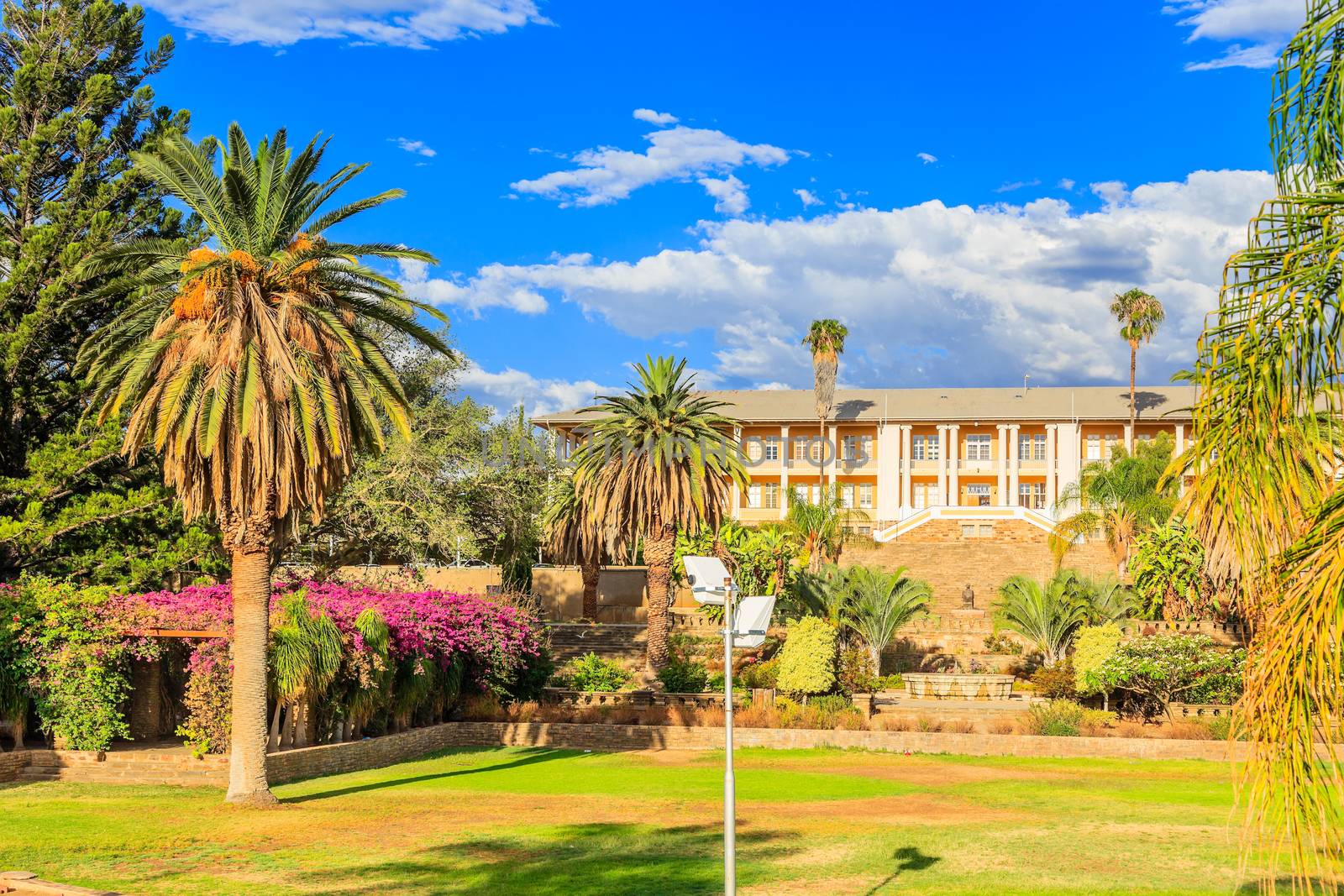 Park and garden with yellow palace building hidden behind tall palms, Windhoek, Namibia