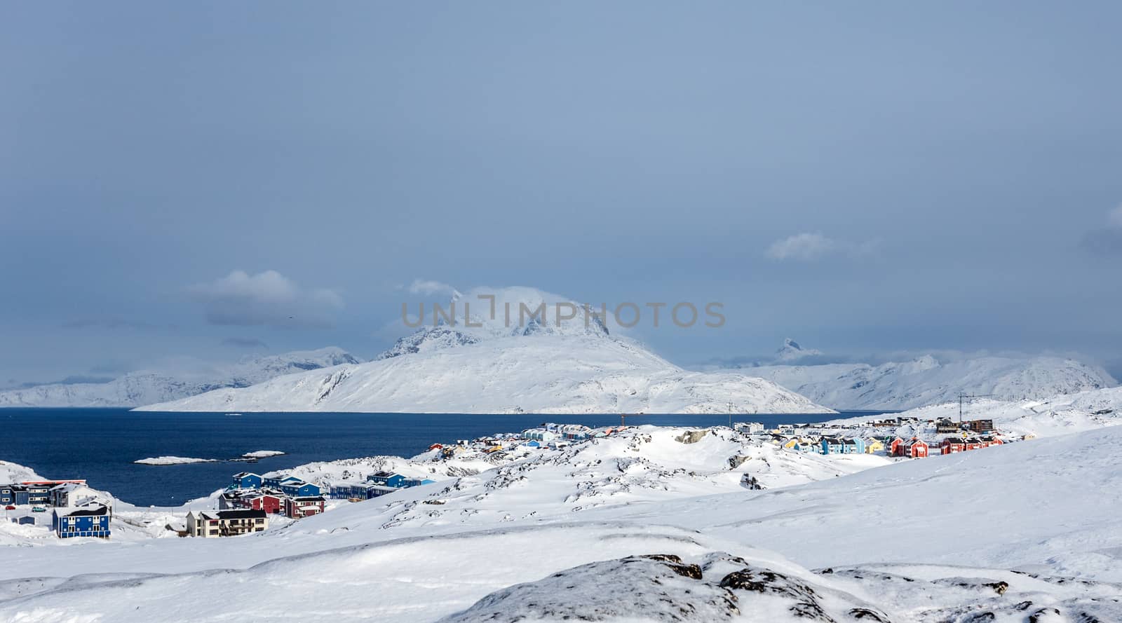 Inuit houses and cottages scattered across tundra landscape in residential suburb of Nuuk city with fjord and mountains in the background, Greenland