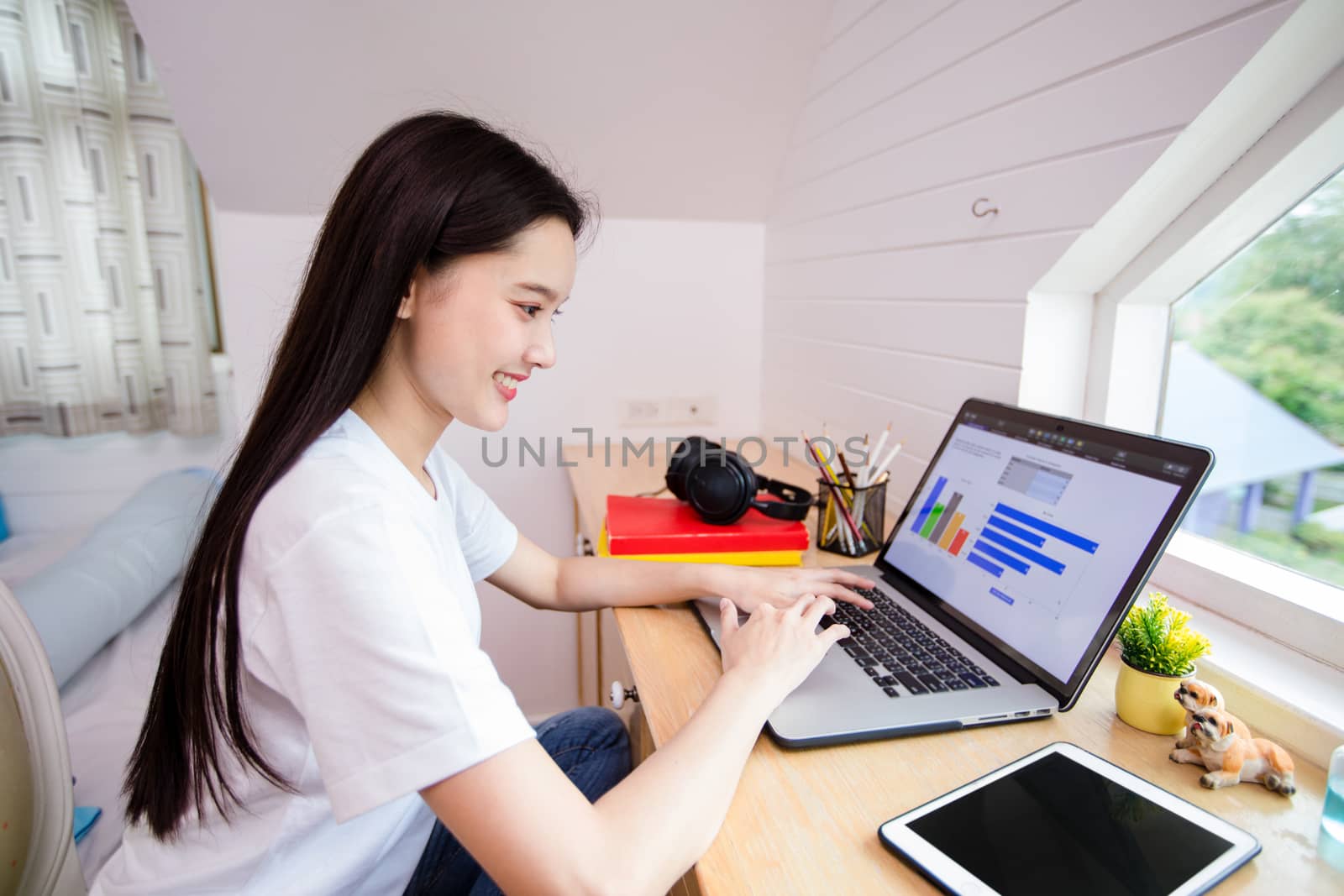 Asian woman happy cheerful cute beautiful is using a notebook computer and sitting on sofa for working from home. She is quarantined at home during the coronavirus epidemic.
