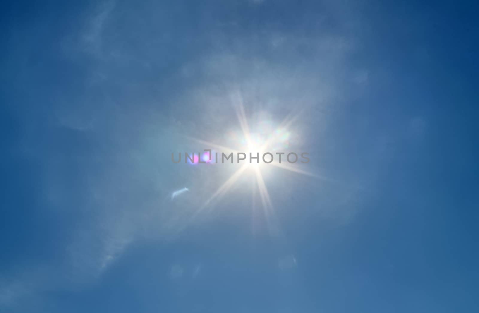 Beautiful view at bright sunbeams with some lens flares and clouds in a blue sky