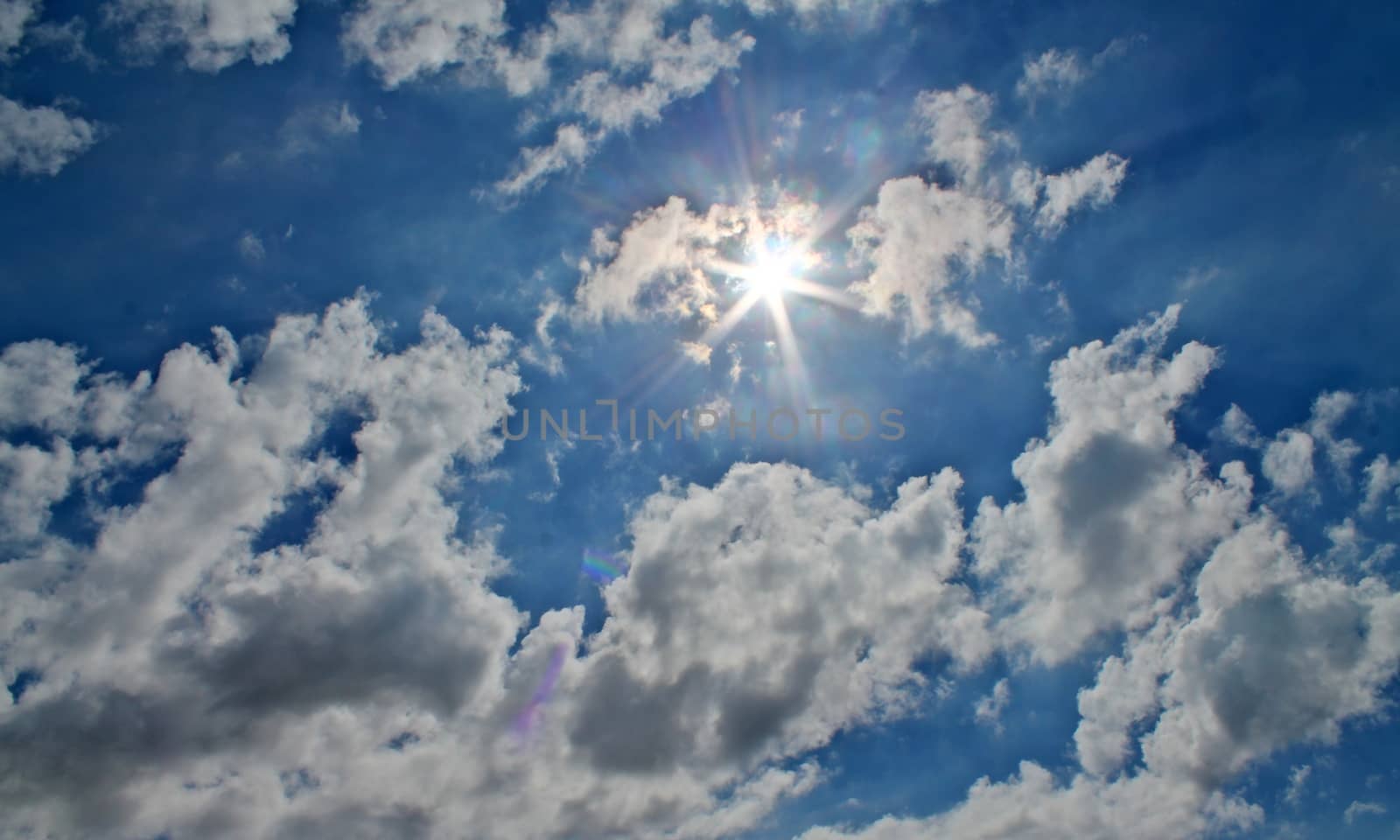 Beautiful view at bright sunbeams with some lens flares and clouds in a blue sky