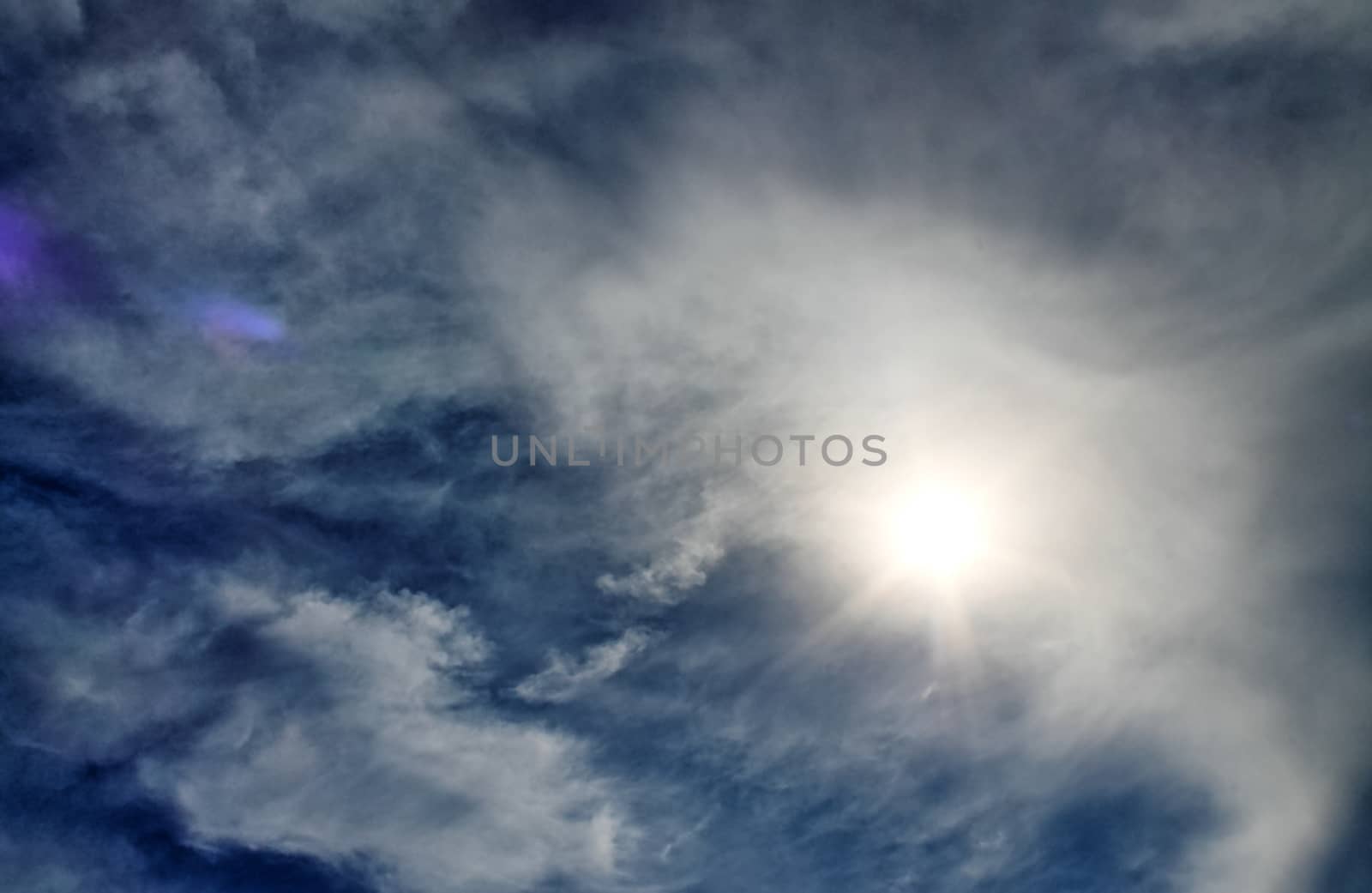 Beautiful view at bright sunbeams with some lens flares and clouds in a blue sky