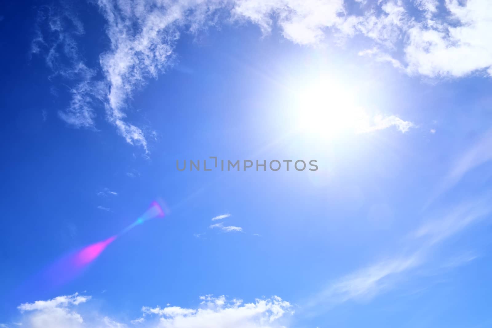 Beautiful view at bright sunbeams with some lens flares and clouds in a blue sky