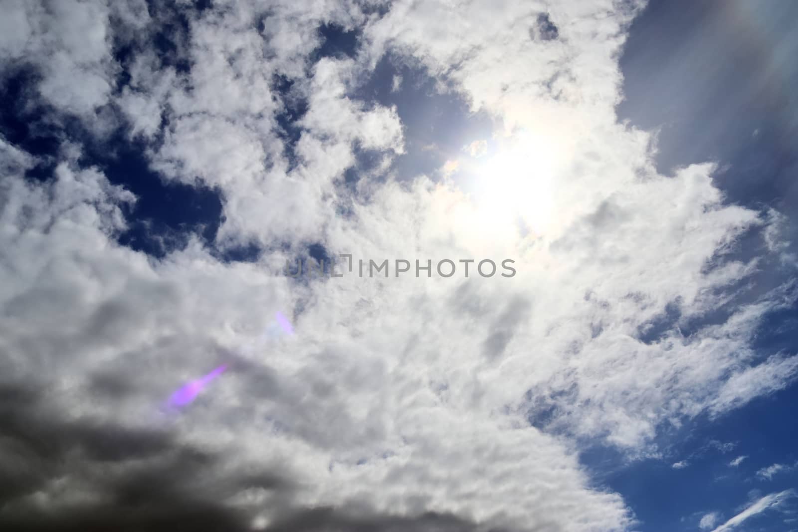 Beautiful view at bright sunbeams with some lens flares and clouds in a blue sky