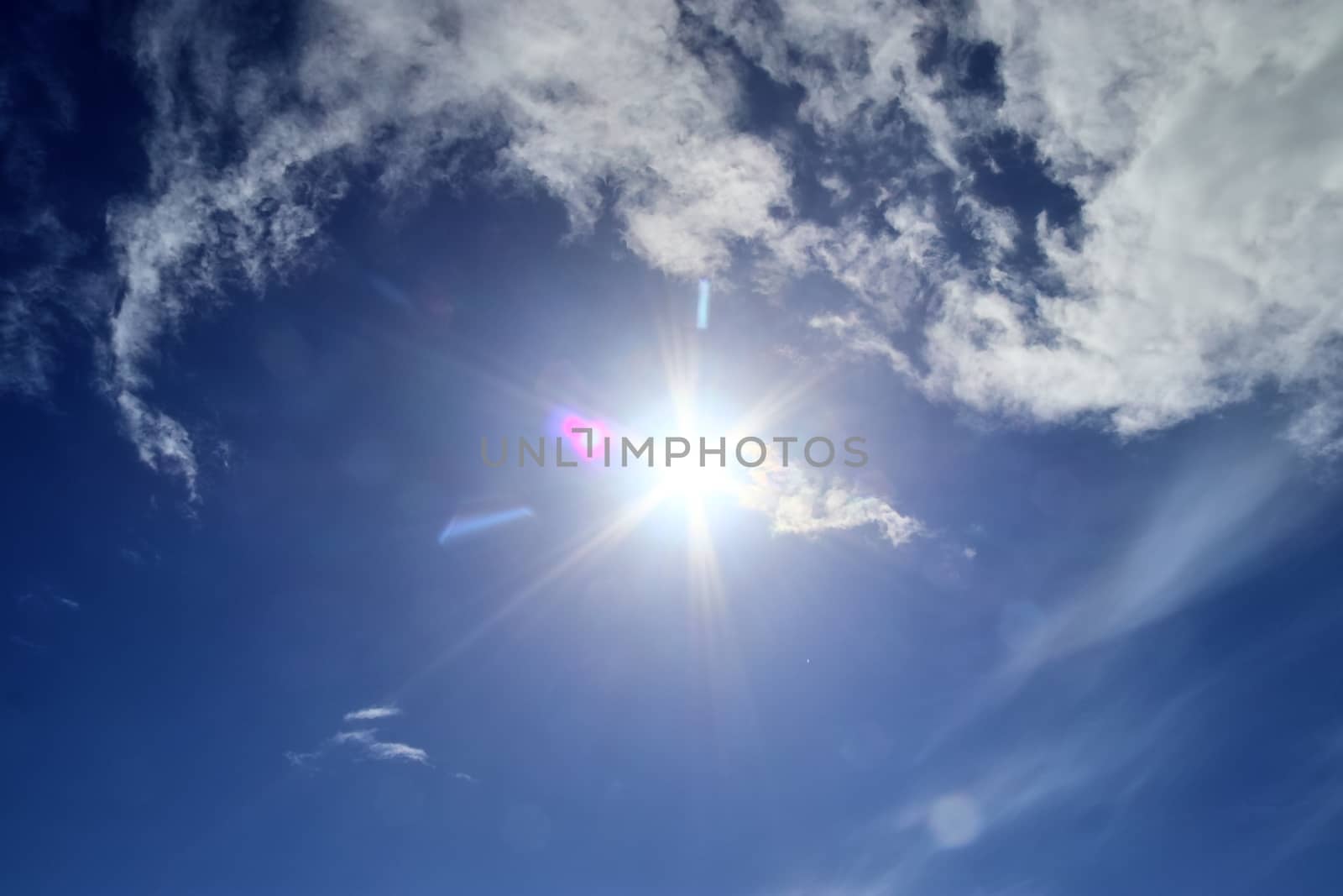 Beautiful view at bright sunbeams with some lens flares and clouds in a blue sky