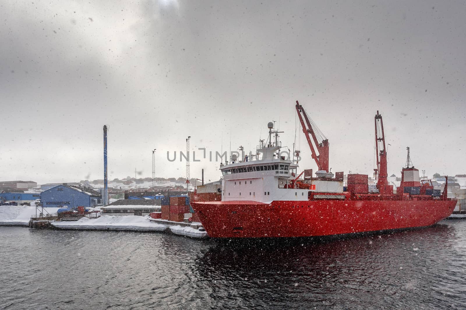 Big red cargo ship under the heavy snowfall in the port of Aasiaat, Greenland