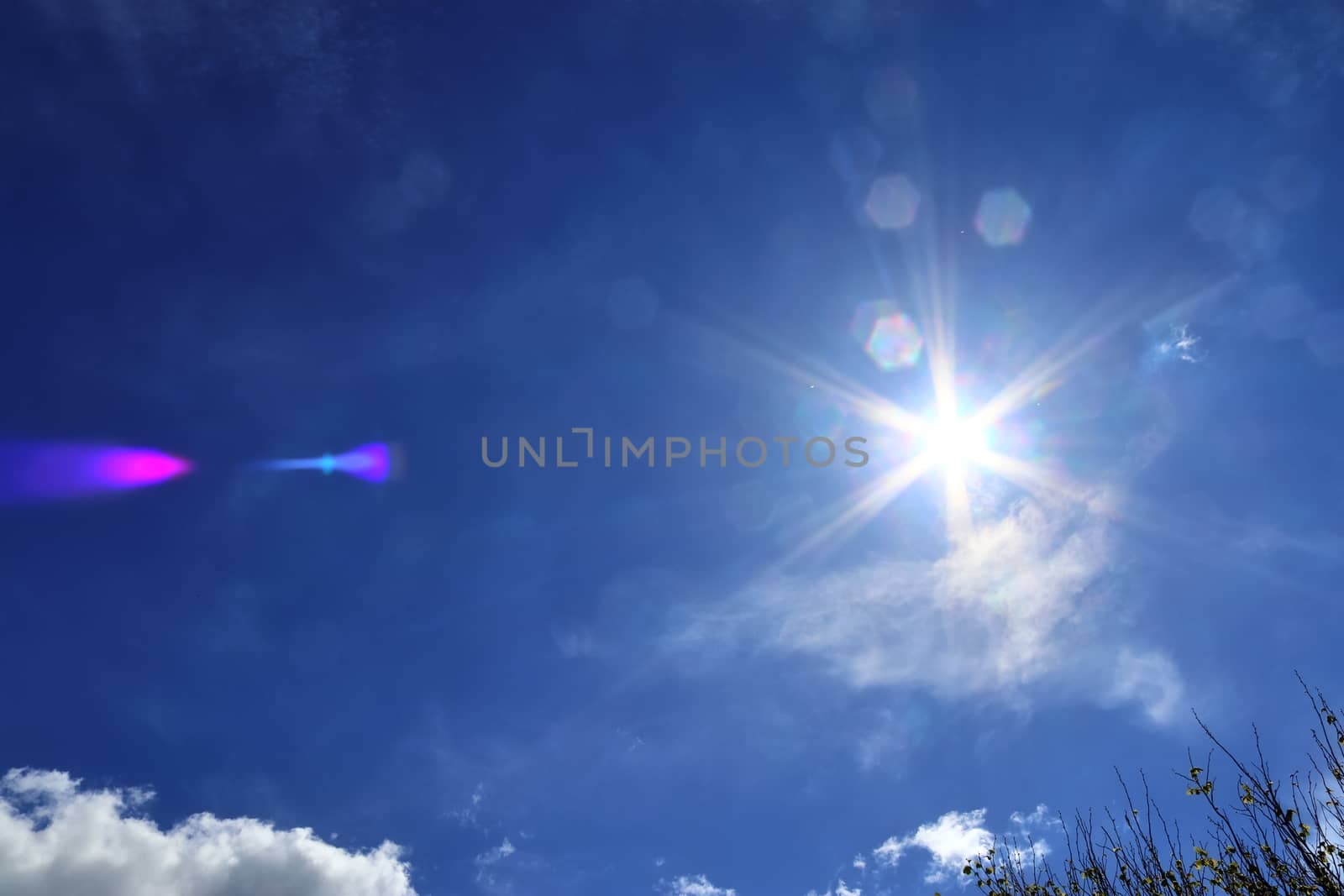 Beautiful view at bright sunbeams with some lens flares and clouds in a blue sky