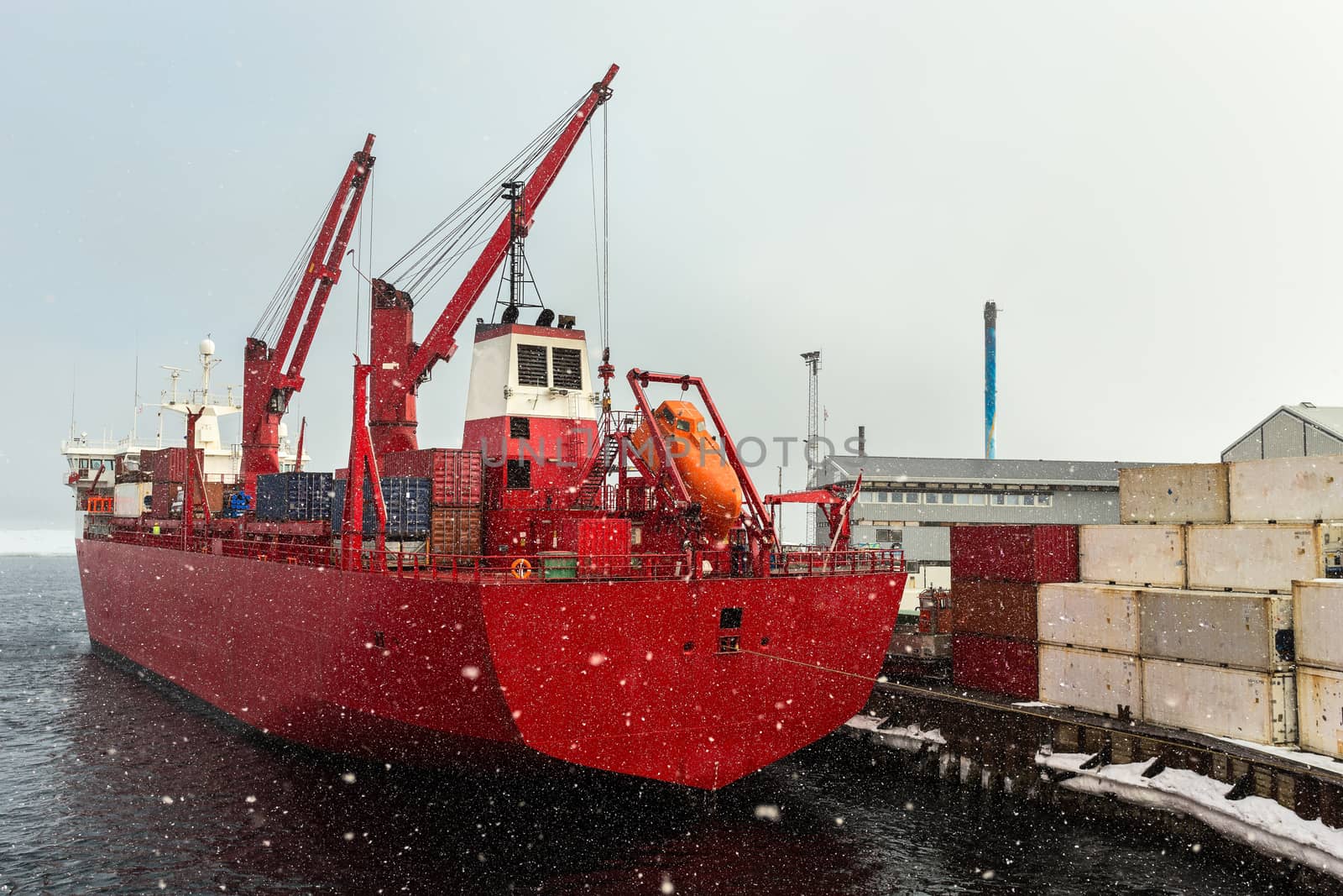 Big red cargo ship under the heavy snowfall in the port of Aasiaat, Greenland