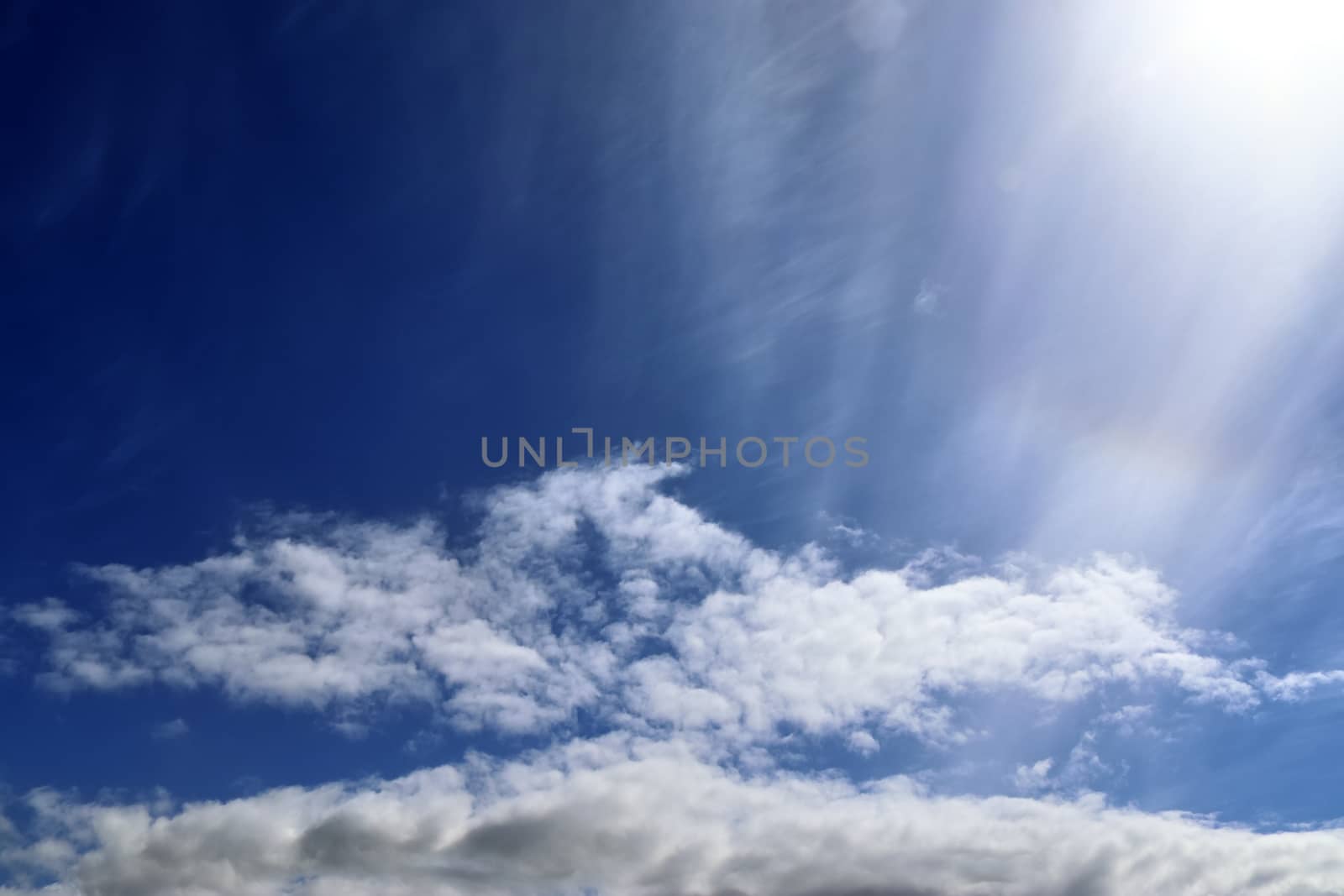 Beautiful view at bright sunbeams with some lens flares and clouds in a blue sky