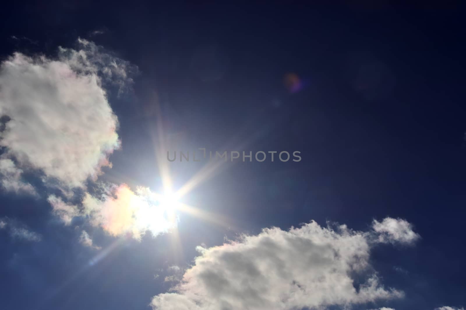 Beautiful view at bright sunbeams with some lens flares and clouds in a blue sky