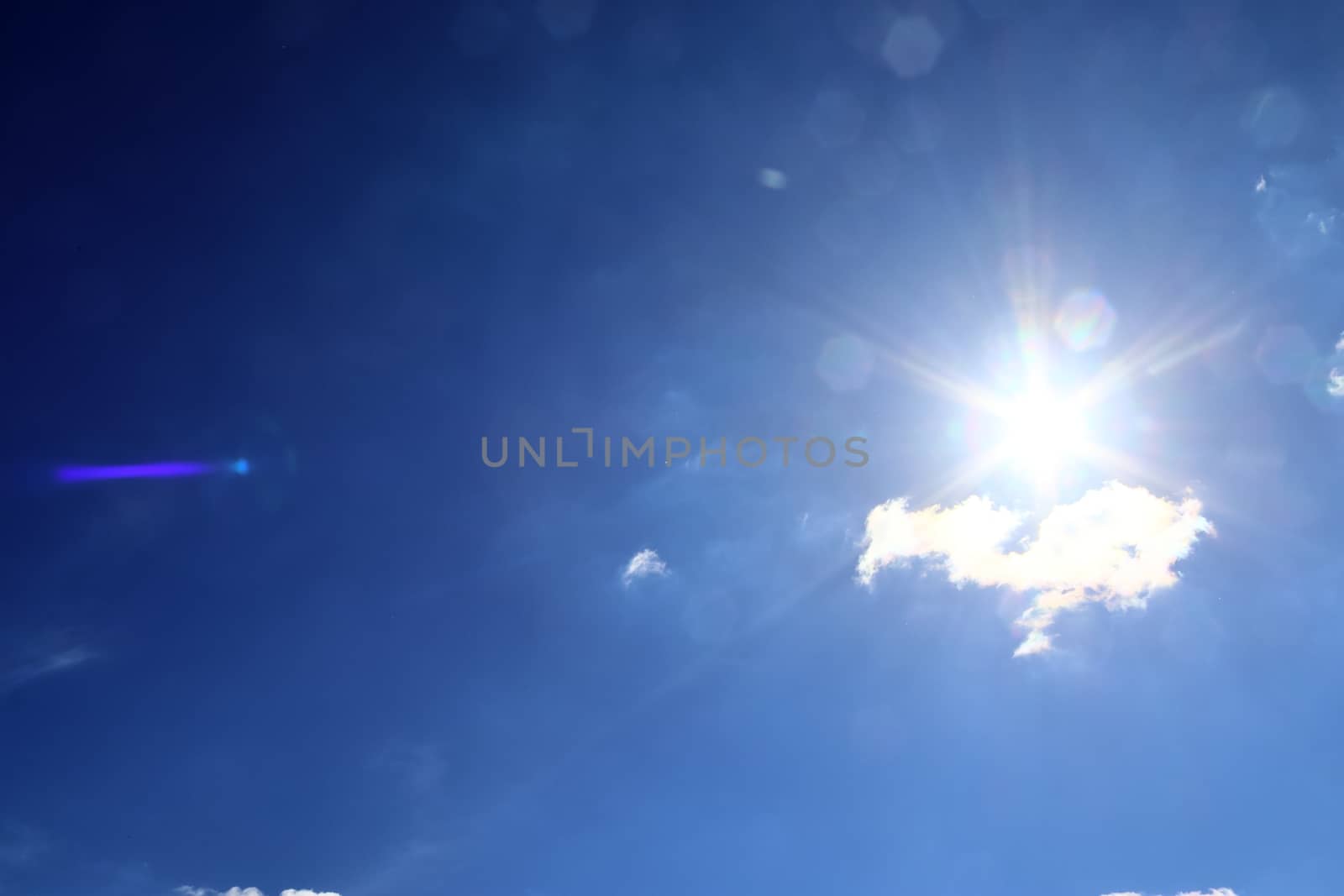 Beautiful view at bright sunbeams with some lens flares and clouds in a blue sky