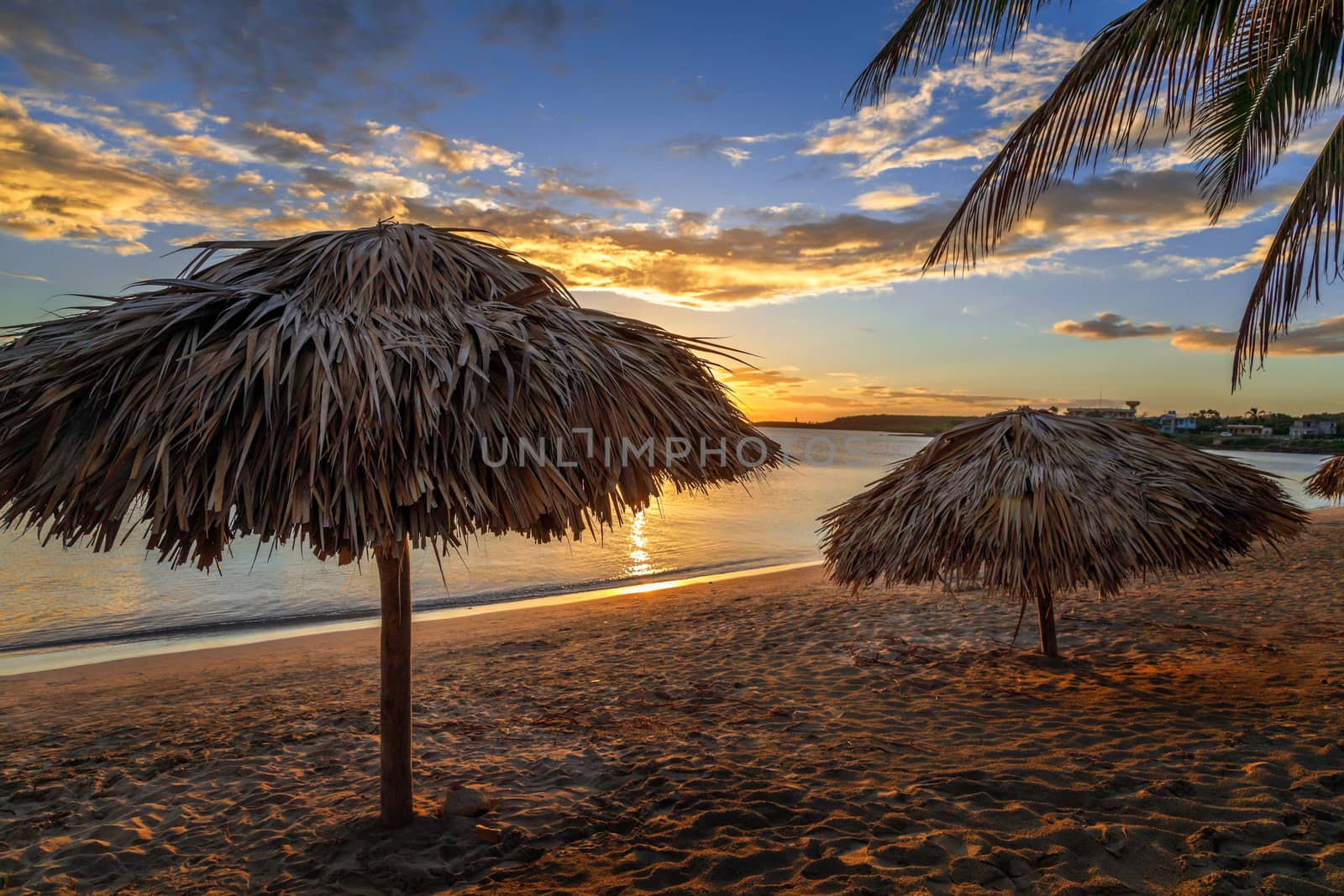 Rancho Luna caribbean beach with palms and straw umbrellas on the shore, sunset view, Cienfuegos, Cuba